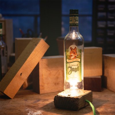 Auf dem Bild ist eine erleuchtete Flasche Fläminger Jagd vor zwei drapierten Holzklötzen zu sehen