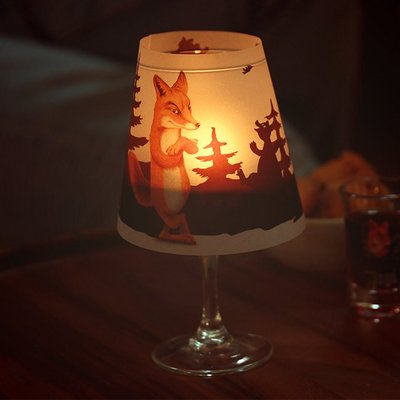 Auf dem Bild ist ein Lampenschirm mit Fuchsmotiv auf einem Weinglas zu sehen