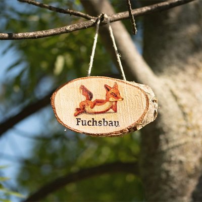 Auf dem Bild ist eine Holzscheibe mit einem Fuchs bemalt zu sehen, die an einem Zweig hängt
